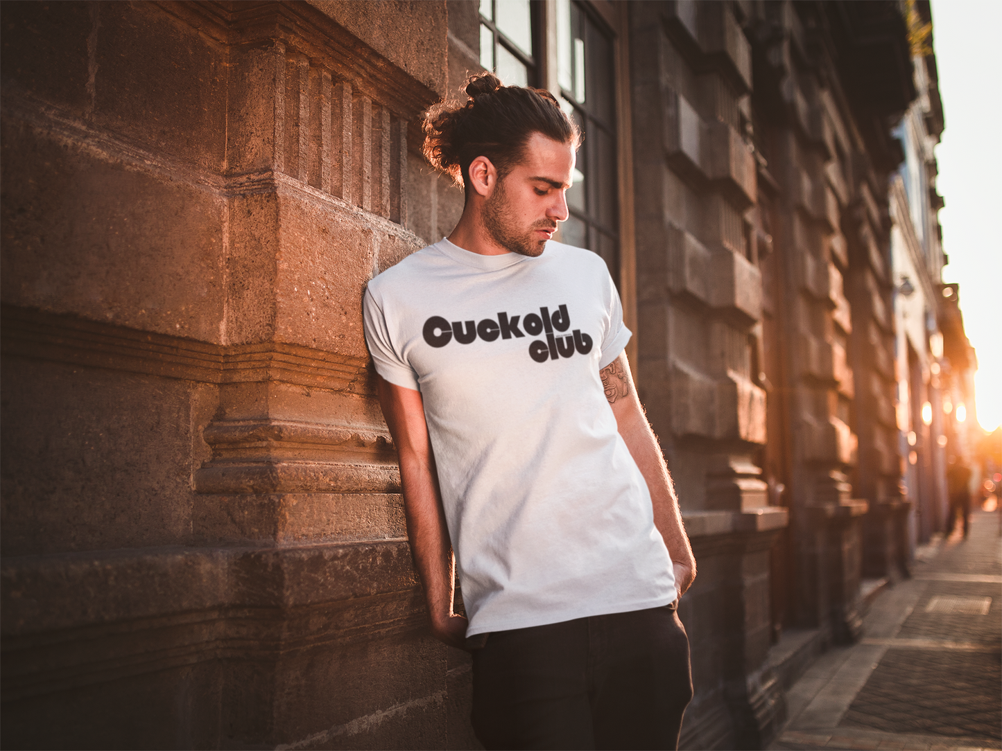 a man leaning against a wall wearing a white t - shirt